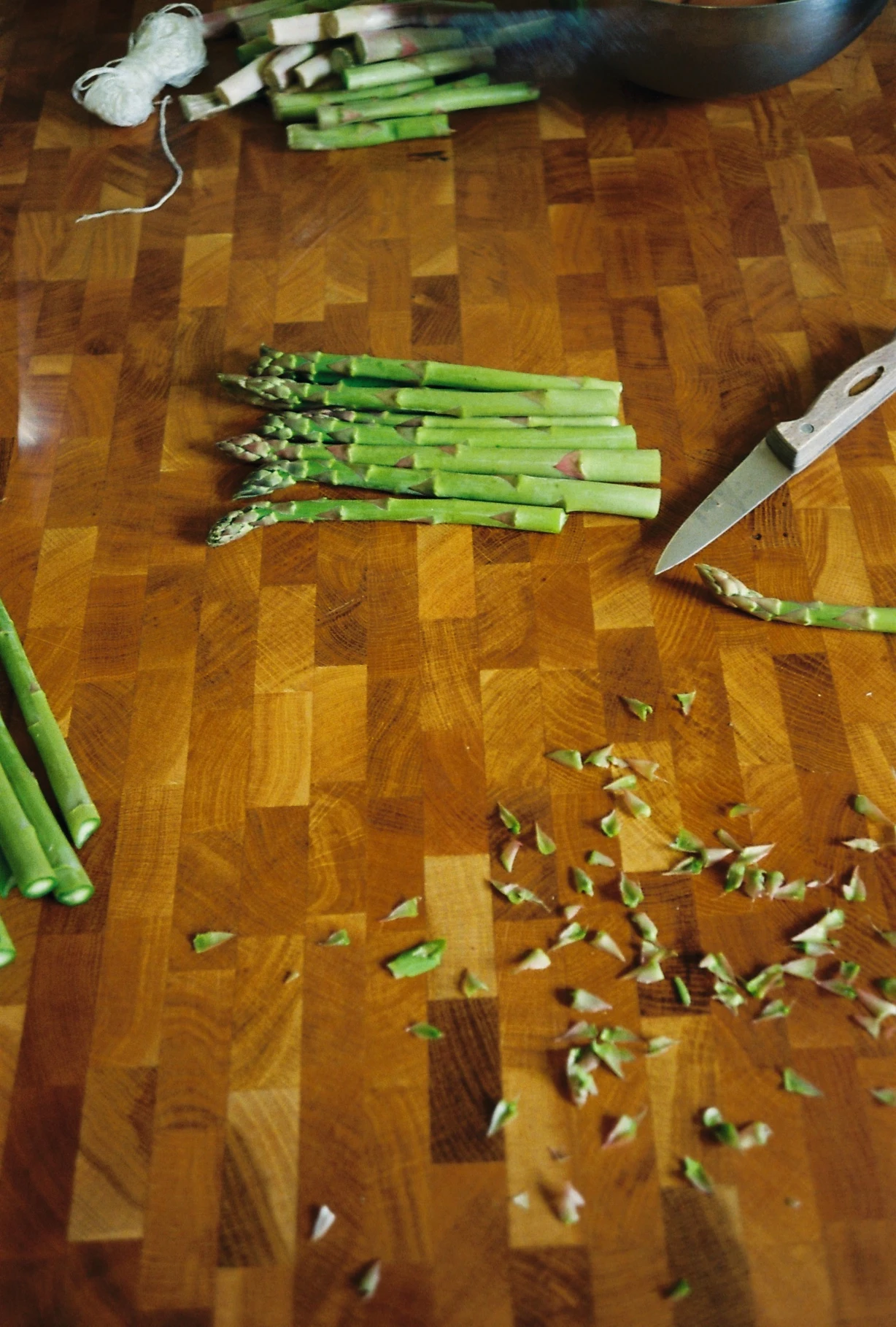 Fresh asparagus spears being trimmed on a wooden cutting board next to a knife and a pile of trimmed tips.