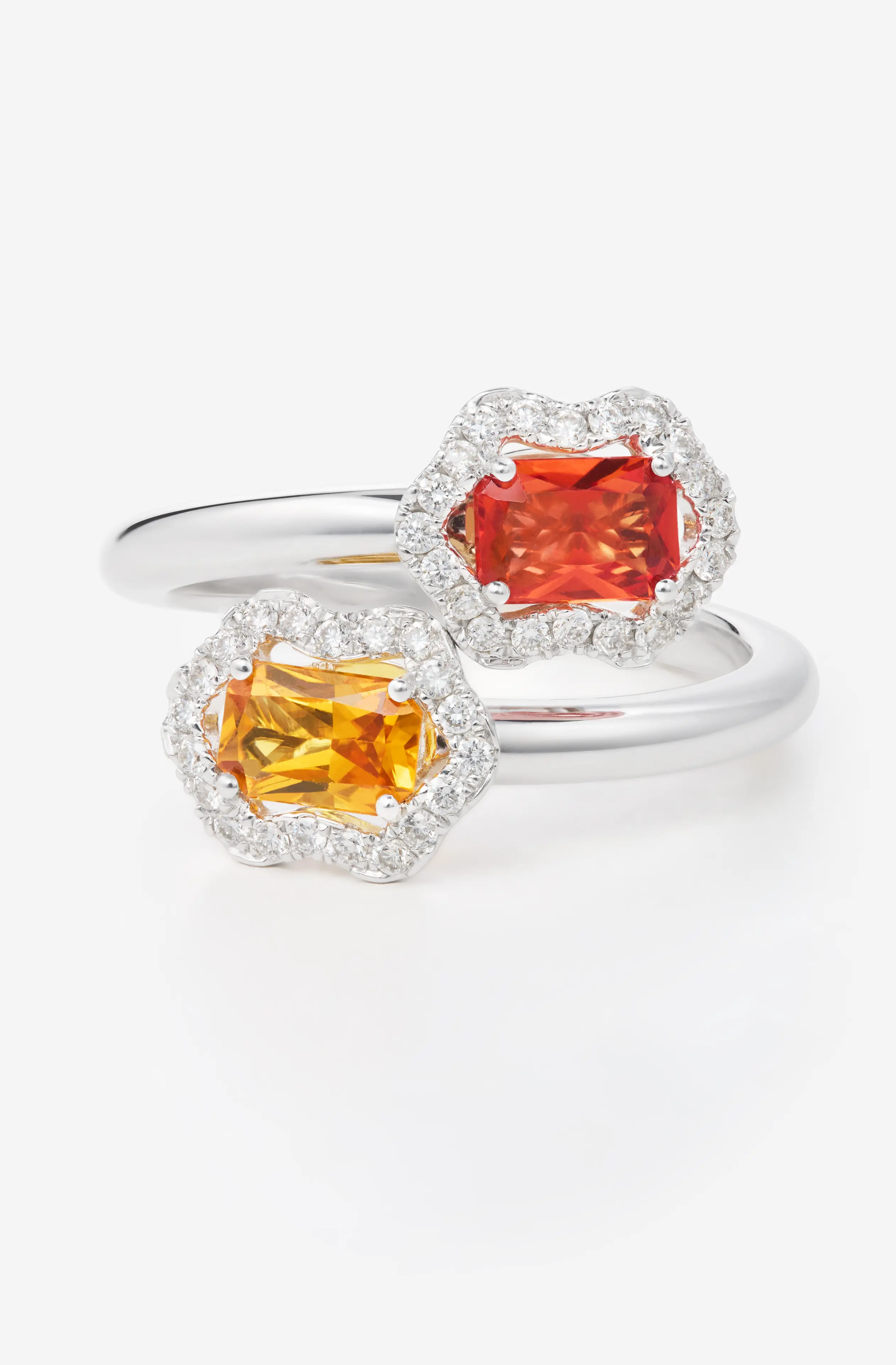 Silver ring with two rectangular gemstones, one orange and one deep red, each surrounded by small diamonds.